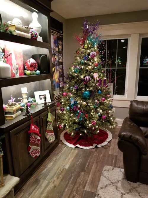 A decorated Christmas tree with colorful ornaments stands next to a shelf adorned with festive decorations and stockings.