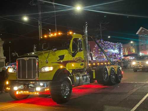 A brightly lit yellow truck with festive decorations drives through a night parade, surrounded by spectators.