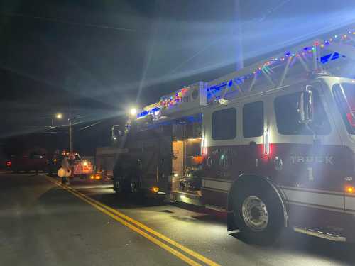 A decorated fire truck parked on a street at night, illuminated by festive lights and street lamps.