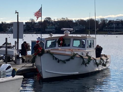 A decorated boat docked by the shore, with people and a dog nearby, and an American flag waving in the background.
