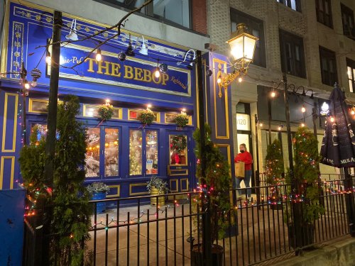 A colorful restaurant exterior decorated with lights and plants, featuring a blue facade and festive holiday decor.