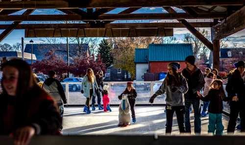 A lively ice skating rink with people of all ages skating and enjoying the winter atmosphere under a wooden structure.