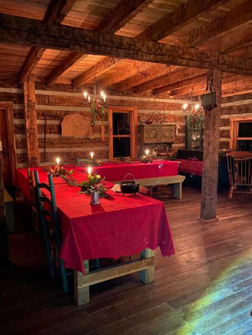 Cozy log cabin interior with red tablecloths, candlelight, and rustic wooden beams, creating a warm atmosphere.