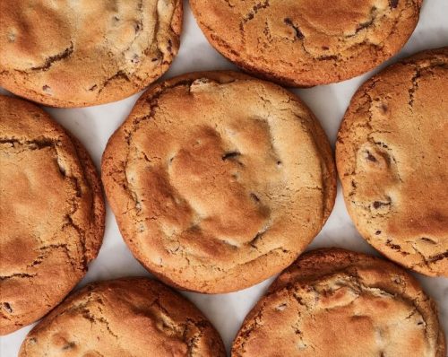 A close-up of freshly baked chocolate chip cookies arranged in a circular pattern on a marble surface.
