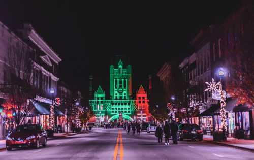 A festive street scene at night, with buildings lit in green and red, and people walking along a decorated avenue.