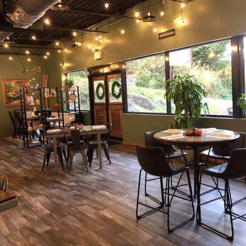 Cozy restaurant interior with wooden tables, chairs, and warm lighting, featuring plants and seasonal decor.