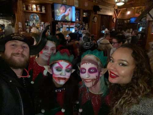 A group of five people in festive costumes with face paint posing together in a lively bar setting.