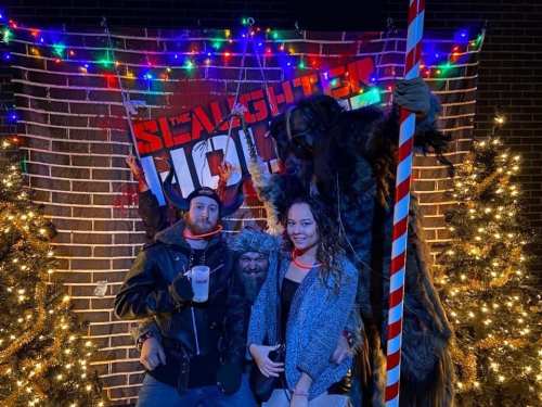 A group of three people poses in front of a festive backdrop with holiday lights and decorations.