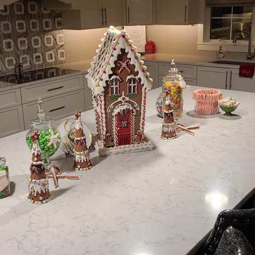 A festive kitchen scene featuring a gingerbread house and decorated candy trees on a marble countertop.