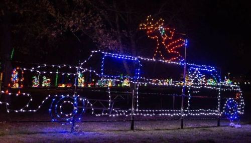 A festive display of a truck outlined in colorful lights, with a reindeer on top, set against a dark night sky.
