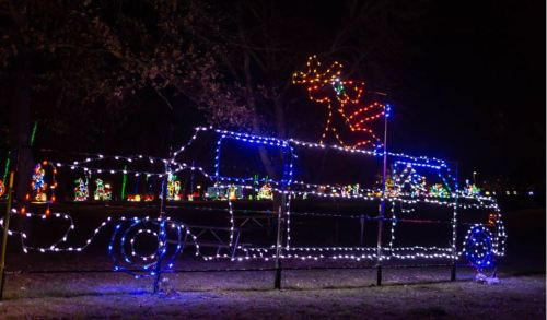 A festive display of colorful lights depicting a truck with a reindeer on top, set against a dark night sky.