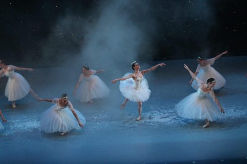 A group of ballet dancers in white tutus performing on stage, surrounded by a misty atmosphere.