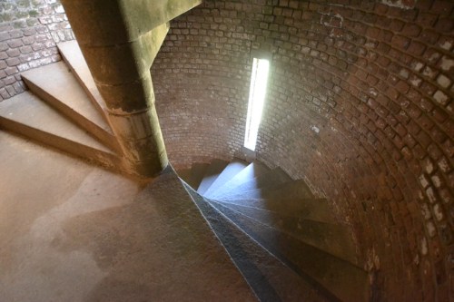 A spiral staircase made of stone and brick, illuminated by a narrow window at the top.