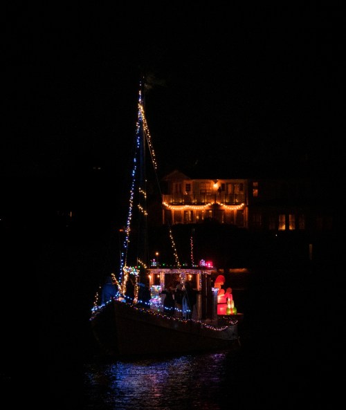 A decorated boat with colorful lights floats on water at night, with festive decorations visible on board.