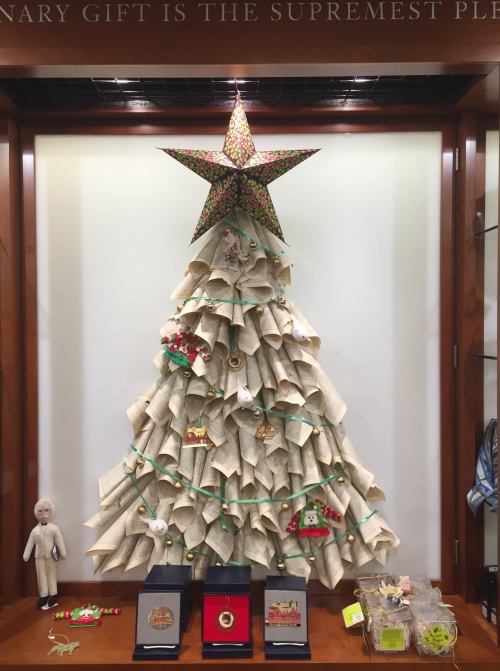 A decorative Christmas tree made of rolled paper, topped with a star, displayed in a glass case with festive ornaments.