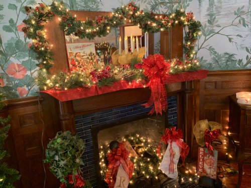 A festive fireplace mantel decorated with greenery, lights, candles, and red bows, creating a warm holiday atmosphere.