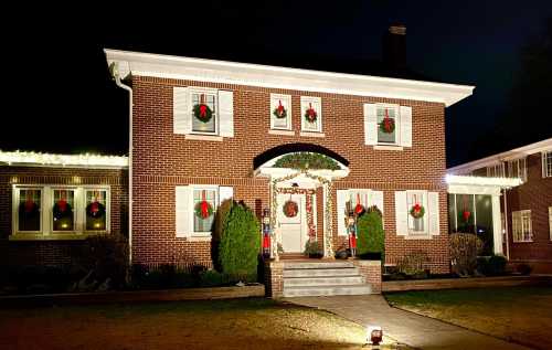 A brick house decorated for Christmas with wreaths, lights, and a festive entrance, set against a night sky.