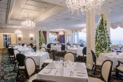Elegant restaurant interior with white tablecloths, chandeliers, and festive decorations, including a Christmas tree.