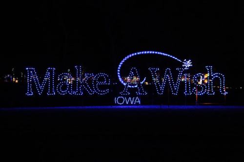 Bright blue holiday lights spell out "Make A Wish Iowa" against a dark background.