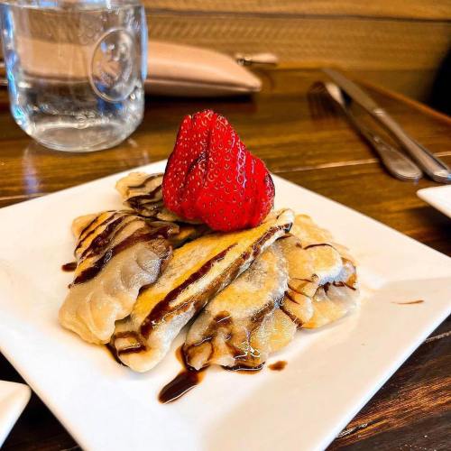 A plate of sweet dumplings drizzled with chocolate sauce, topped with a fresh strawberry.