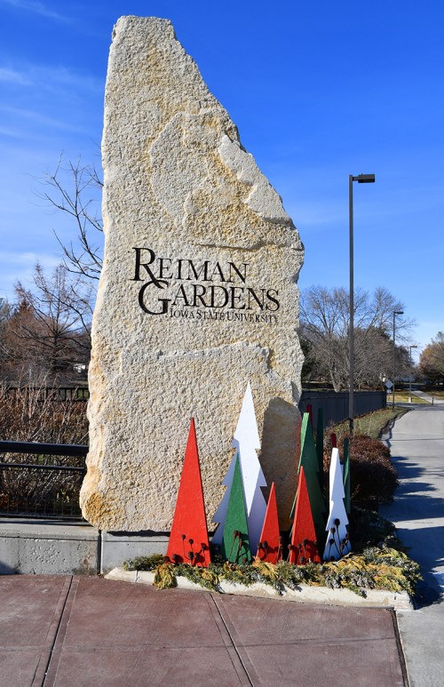 Sign for Reiman Gardens at Iowa State University, featuring colorful holiday decorations in front of a large stone.