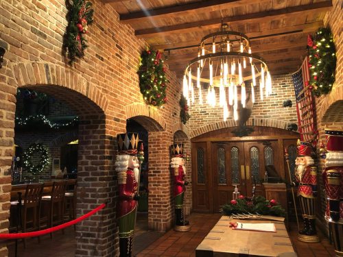 Cozy brick interior decorated for the holidays, featuring nutcracker figures, wreaths, and a chandelier.