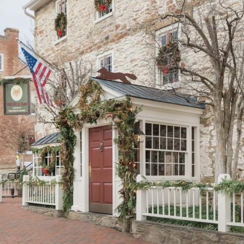 A historic stone building decorated with greenery and a red door, featuring an American flag and festive accents.