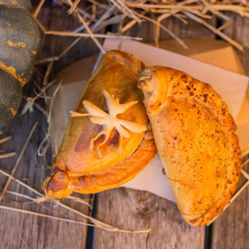 A close-up of two baked empanadas on a rustic wooden surface, with a decorative pumpkin in the background.