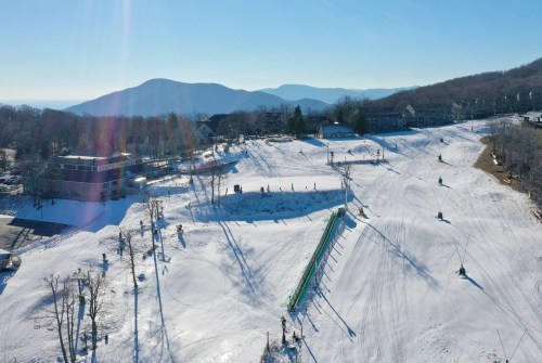 A snowy ski resort with slopes, ski lifts, and mountains in the background under a clear blue sky.