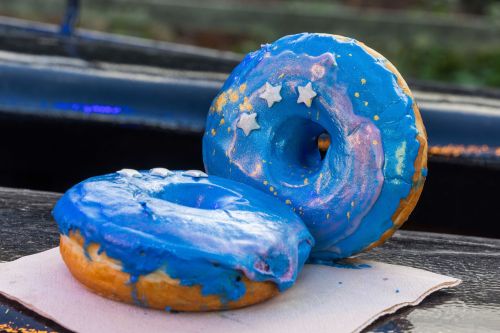 Two colorful donuts with blue icing and star decorations, resting on a napkin against a blurred background.