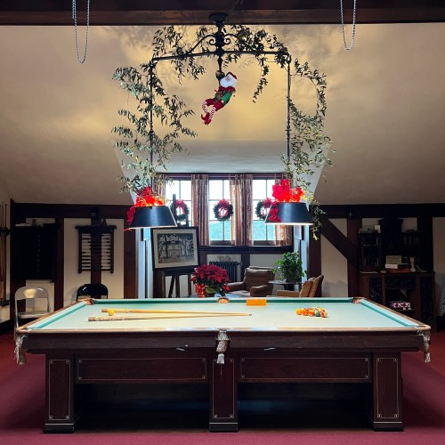 A cozy game room with a pool table, festive decorations, and a chandelier adorned with greenery and ornaments.