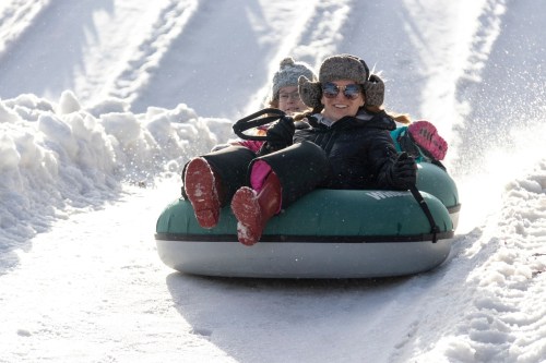 A group of people joyfully tubing down a snowy slope, wearing winter gear and smiling as they slide.