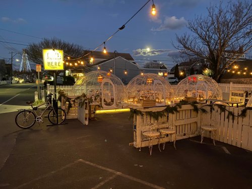 Outdoor dining area with illuminated igloo-style tents, string lights, and a bicycle parked nearby at dusk.