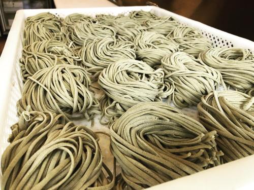 A close-up of neatly arranged bundles of green pasta in a white basket.