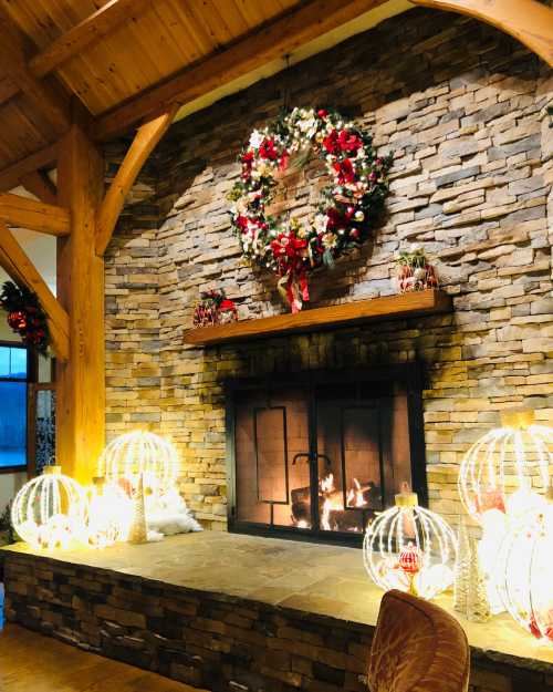 Cozy fireplace with a stone wall, decorated with a festive wreath and illuminated ornaments for a warm holiday atmosphere.