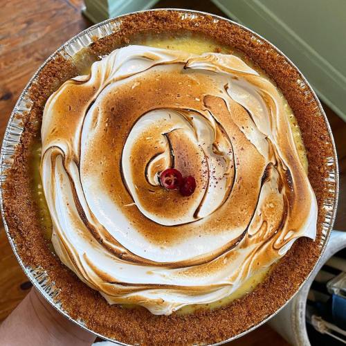 A close-up of a beautifully baked pie with a golden-brown meringue swirl and a graham cracker crust, topped with a berry.