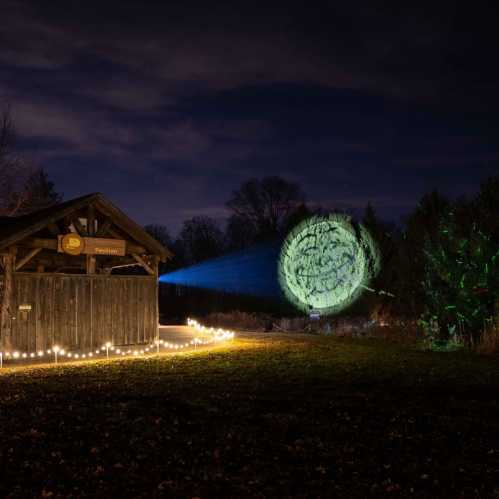 A wooden building with a sign, illuminated by string lights, under a starry sky with a green light projection nearby.