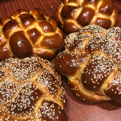 A variety of freshly baked braided breads, some topped with sesame seeds, arranged on a wooden surface.