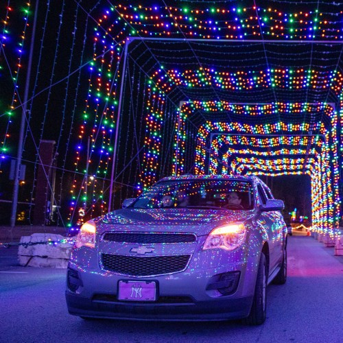 A car drives through a colorful tunnel of bright, multicolored lights at night.