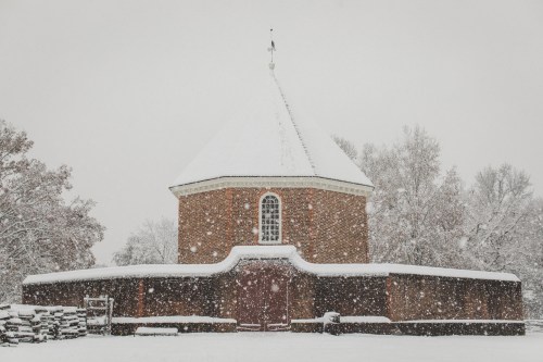A snow-covered round brick building surrounded by trees, with large windows and a snowy landscape.