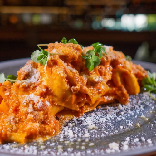 A plate of pasta topped with a rich tomato sauce, herbs, and grated cheese, served on a dark plate.