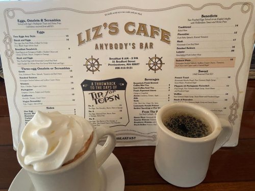 A menu from Liz's Cafe featuring breakfast items, with a cup of coffee and a dessert in front.