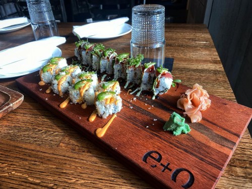 A wooden platter with various sushi rolls, garnished with wasabi, pickled ginger, and drizzled sauces.