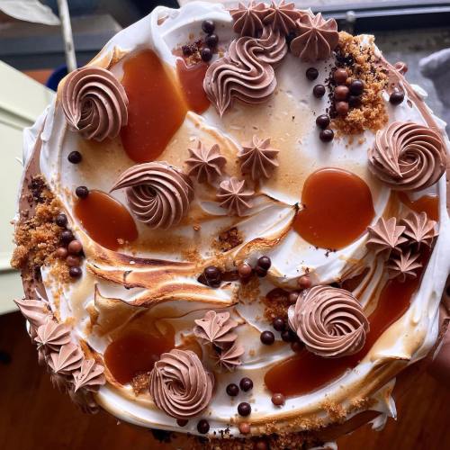 A decadent cake topped with swirls of chocolate frosting, caramel drizzle, and decorative chocolate balls.