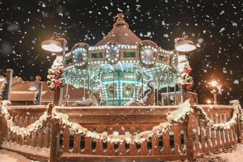 A beautifully lit carousel adorned with festive decorations, surrounded by snow and falling snowflakes at night.