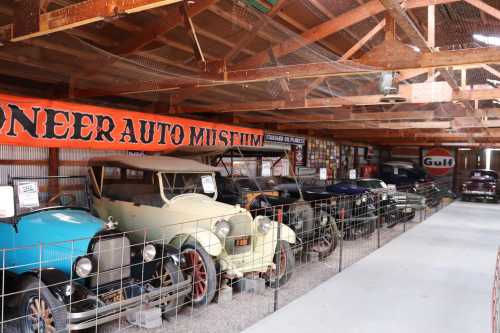 A row of vintage cars displayed in a rustic auto museum with a banner overhead.