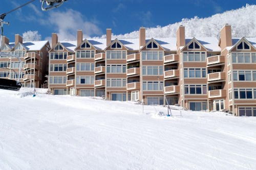A row of ski resort condos with large windows, set against a snowy landscape and blue sky.