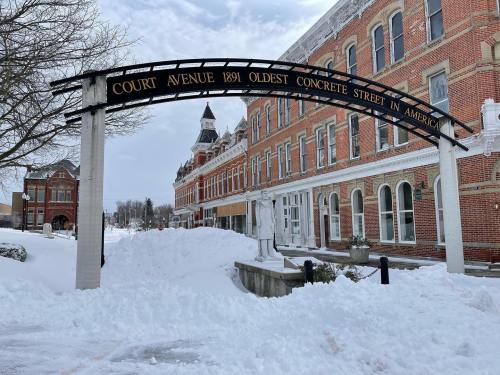 Archway sign reading "Court Avenue 1891 Oldest Concrete Street in America" with snow-covered buildings in the background.