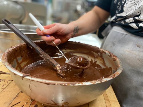 A hand holding a spatula mixes melted chocolate in a large bowl, with baking tools in the background.