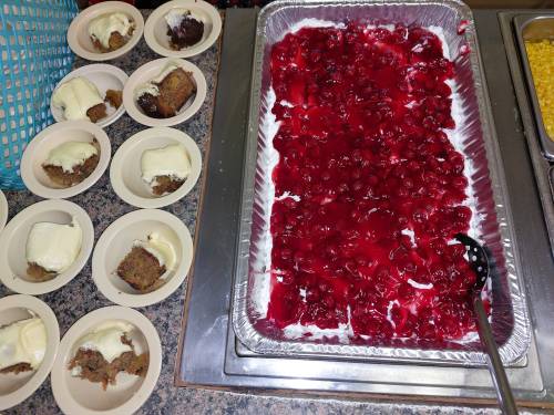 A tray of cherry dessert next to plates of cake topped with ice cream.